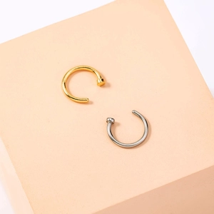 Detailed view of U-shaped gold and silver nose rings on a beige geometric display stand