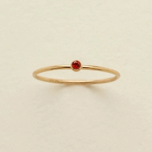 Primer plano de un anillo de oro minimalista con una gema roja redonda única