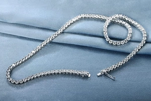 Detailed close-up of a silver tennis necklace with sparkling cubic zirconia on blue silk