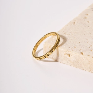 Minimalist gold stainless steel ring with delicate flower engravings on stone background
