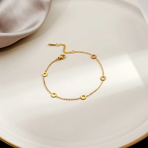 Detail of gold chain bracelet with gear charms on white plate and purple silk background