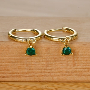 Elegant gold hoop earrings with sparkling green zircon pendant on natural wood base
