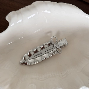 Detail of silver metallic ribbon bow hair clip with hammered texture in shell dish