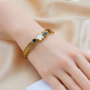 Gold-plated clover bangle with black and white inlay worn against silk fabric
