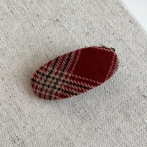 Detail shot of vintage red and black plaid fabric texture on oval hair clip on linen background