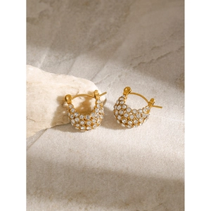 Détail de boucles d'oreilles en or 18k avec strass brillants sur une surface en pierre
