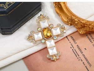 Close-up of vintage gold cross brooch with yellow gemstone and floral fleur-de-lis details