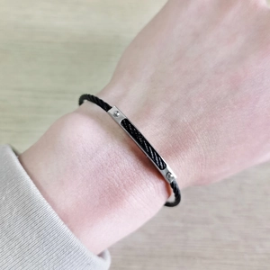 Close-up of black braided steel cable bracelet with rectangular silver metal plate