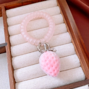 Primo piano di elastico a spirale rosa con ciondolo a fragola floccata in portagioie di velluto