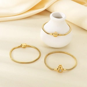Three gold snake bone bracelets with heart, shell, and diamond crown clasps on silk