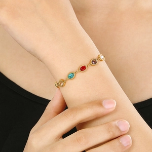Detail of a gold stainless steel bracelet with colorful oval gemstones on a wrist