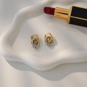 Detail of minimalist two-tone linked earrings on a white ceramic tray with lipstick