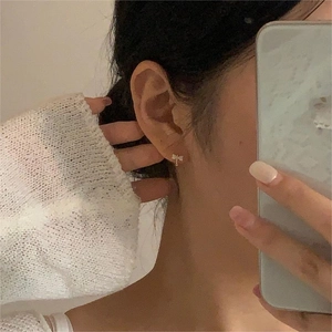 Detailed macro view of small gold-rimmed bow stud earrings worn by a model in mirror selfie
