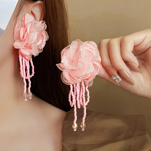Close-up of pink fabric flower earrings with long beaded tassels on model's ear