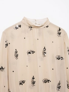 Detail of high collar with fabric buttons and sequined floral embroidery on beige chiffon blouse