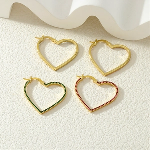 Flat lay of gold heart earrings with red and green rhinestones on textured white background