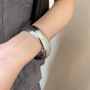 Gros plan d'un large bracelet manchette argenté minimaliste avec finition polie miroir