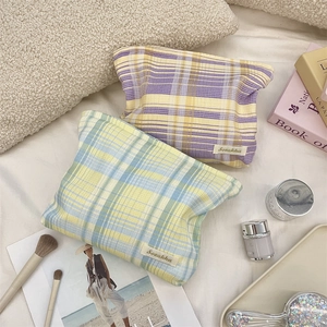Close-up of pastel checkered makeup bags in soft fabric on cozy bedding