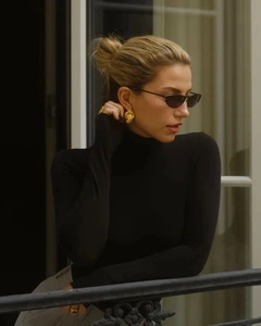 Close-up of elegant 18K gold scarf knot earrings worn with a chic black turtleneck outfit