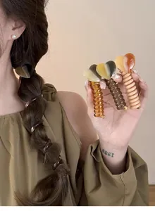 Three heart-shaped spiral hair ties in amber, green and pink on a female model
