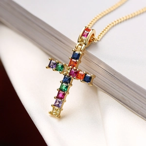 Macro shot of gold cross necklace with multicolored square-cut gems on white silk fabric