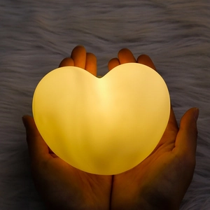 Heart-shaped LED night light held in hands with warm glow on white faux fur background