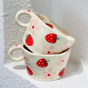 Detail of stacked handmade ceramic mugs featuring hand-painted strawberry and flower patterns