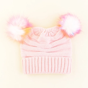 Close-up of pink knit kids hat featuring colorful dual faux fur pom-poms on creamy background