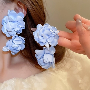 Détail de boucles d'oreilles fleurs en satin bleu portées par un mannequin chic