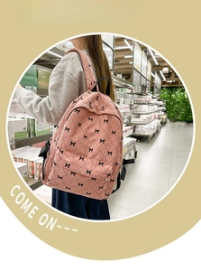 Pink corduroy backpack with bow embroidery worn by a student in a bright aisle