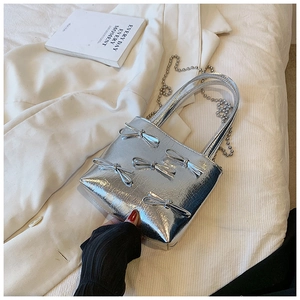 Detail of silver pleated handbag with 3D bows and metallic chain strap on white fabric