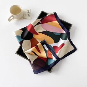 Artistic layout of a multicolored silk square scarf on a black tray with a soft aesthetic