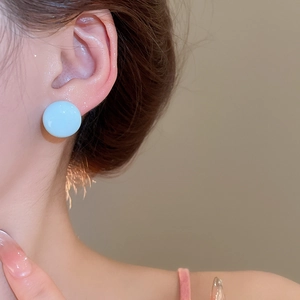 Close-up of light blue round stud earrings with smooth surface and sweet style