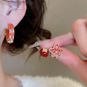 Close-up of asymmetric cherry and maple leaf earrings with red zircon in gold finish