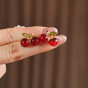 Close-up of a cherry-shaped resin earring featuring red beads and golden leaf details