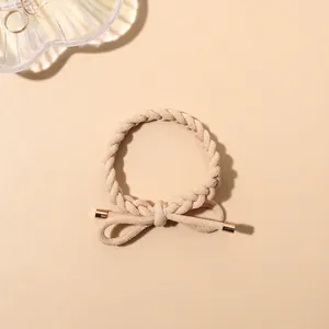 Detail of beige braided hair tie featuring a twisted rope design and gold tipped bow accent