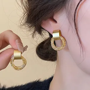 Golden irregular droplet earrings featuring multi-layered textured rings on a model