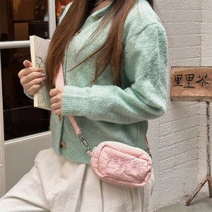 Close-up of pink crossbody bag with embroidered bow detail and chain fabric strap