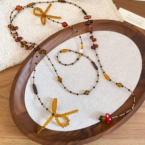 Detail of beaded long necklace with amber bows, mushroom charm, and vintage beads