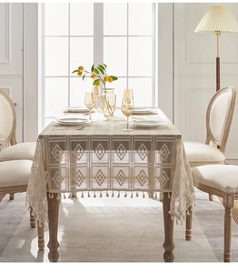 Close-up of beige crochet lace tablecloth with geometric patterns and tassel fringe edge