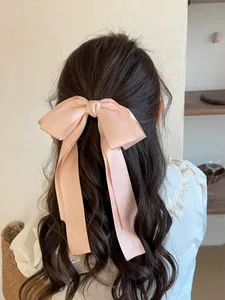 Nœud géant en satin rose avec longs rubans porté sur des cheveux longs bouclés