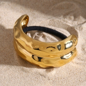 Golden wavy stainless steel hair tie accessory with black elastic band on sandy beach