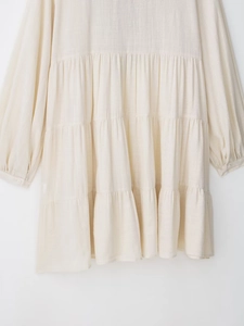 Detail of tiered ruffled cream dress featuring cotton linen texture and buttoned cuffs