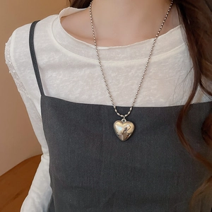 Close-up of a silver heart pendant necklace with a polished finish on a beaded chain