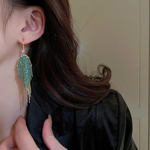 Close-up of long gold chain tassel earrings with green rhinestones worn by a model