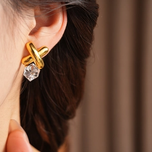 Close-up of vintage gold cross earrings with faceted crystal drop charms on model