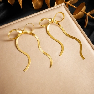 Elegant gold bow earrings with metal tassels on a luxury display stand for women