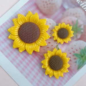 Three glossy yellow resin sunflower DIY accessories in various sizes on a pink card