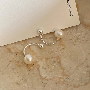 Detail of 925 sterling silver C-shape earring with a white pearl on marble surface