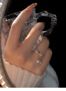 Detailed view of gold plated bow ring with hanging pearl tassel on model's finger